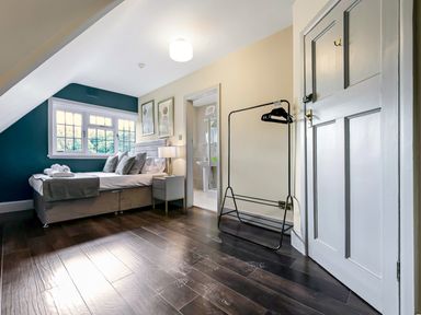 A bedroom with a bed, nightstand with lamp, window, clothes rack, and a door leading to a bathroom at Tudor Grange in Bournemouth