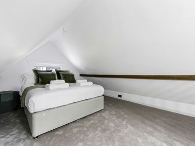 A bedroom with a bed pillows and towels under a slanted ceiling with a wooden beam at Tudor Grange in Bournemouth