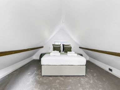 A bedroom with a bed centered under a sloped ceiling and wooden beams at Tudor Grange in Bournemouth