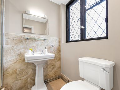 A bathroom with a pedestal sink a toilet a mirror and a window with lattice design at Tudor Grange in Bournemouth