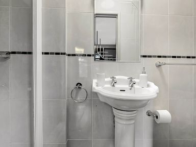 A bathroom with a pedestal sink a mirror and tiled walls at Tudor Grange in Bournemouth