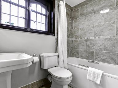 A bathroom with a bathtub with towel a toilet and a sink under a window at Tudor Grange in Bournemouth
