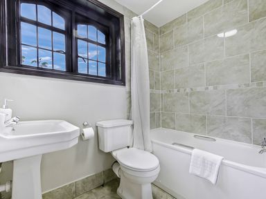 A bathroom with a sink toilet bathtub with shower curtain and a window showing blue sky at Tudor Grange in Bournemouth