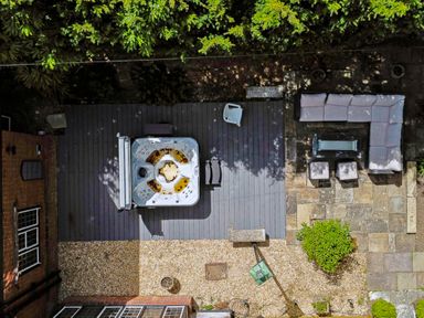 An outdoor area with a hot tub on wooden decking a patio with L shaped sofa stools and a fire pit at Tudor Grange in Bournemouth