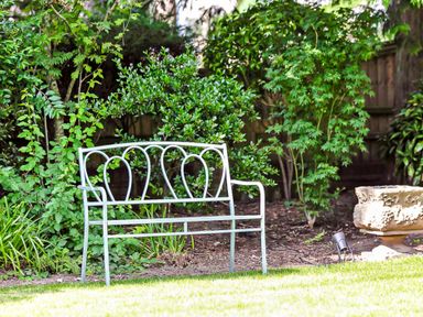 A metal garden bench and a stone planter among green bushes in a backyard at Tudor Grange in Bournemouth