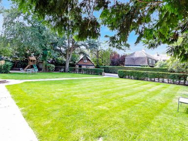 A green lawn with a play structure and chairs near houses and trees at Tudor Grange in Bournemouth