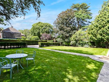 A garden with a round table and four chairs on the grass and a paved pathway at Tudor Grange in Bournemouth