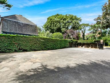 An outdoor paved area with a hedge fence and trees surrounding a building at Tudor Grange in Bournemouth