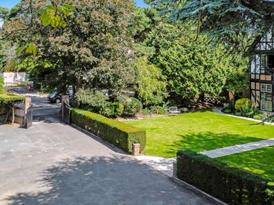 A garden with a lawn bench trees and hedges near a driveway at Tudor Grange in Bournemouth