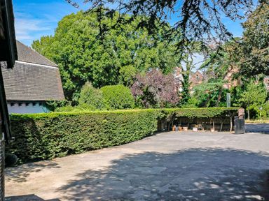 An outdoor paved area with a hedge and trees surrounding it at Tudor Grange in Bournemouth