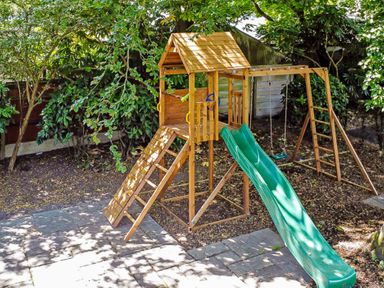 A wooden play structure with a slide and swings in a garden at Tudor Grange in Bournemouth