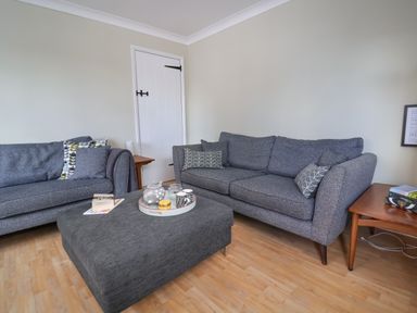 A living room with two gray sofas a gray ottoman table and wooden side tables at 8 Biddlecombe Orchard in Bridport