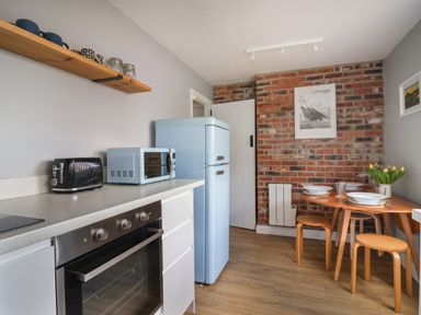 A kitchen with a blue refrigerator microwave black toaster and a dining table with chairs and yellow flowers at 8 Biddlecombe Orchard in Bridport