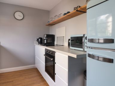 A kitchen with white cabinets a black oven a blue refrigerator a microwave and a countertop with small appliances at 8 Biddlecombe Orchard in Bridport