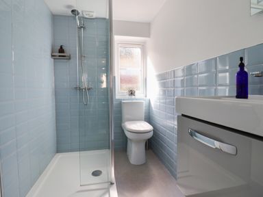 A bathroom with a shower, toilet, sink, and blue tiled walls at 8 Biddlecombe Orchard in Bridport