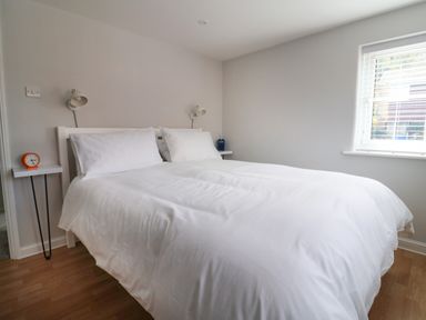 A bedroom with a white bed and pillows two wall-mounted lamps and a window with blinds at 8 Biddlecombe Orchard in Bridport
