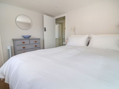 A bedroom with a white bed and pillows a gray dresser with a blue bowl and a round mirror on the wall at 8 Biddlecombe Orchard in Bridport