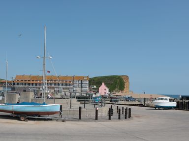 A harbor with boats on trailers a pink house near a cliff and a large building at 8 Biddlecombe Orchard in Bridport