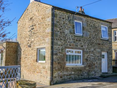 A stone house with white framed windows and a white door on a paved street at Bridge End Cottage in Wark