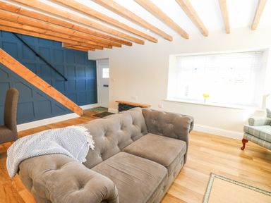 A living room with a grey sofa a blue accent wall with stairs and a window with blinds at Bridge End Cottage in Wark