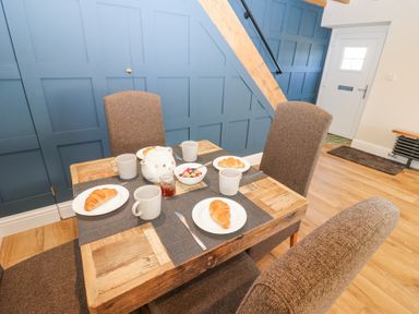 A dining table set with cups plates croissants a teapot and fruit bowl with chairs in a room with blue paneled walls at Bridge End Cottage in Wark