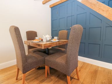 A dining area with a wooden table and four chairs set with teapot cups and croissants at Bridge End Cottage in Wark