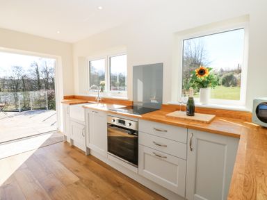 A kitchen with wooden countertops a sink an oven a bottle with glasses and a sunflower in a vase at Bridge End Cottage in Wark