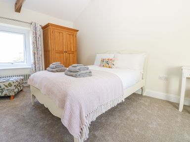 A bedroom with a bed, towels, wooden wardrobe, window with floral curtains, and butterfly ottoman at Bridge End Cottage in Wark