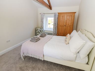 A bedroom with a bed folded towels an armchair a wooden wardrobe and a window at Bridge End Cottage in Wark