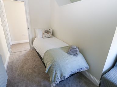 A small bedroom with a single bed a patterned throw pillow and folded towels on the bed at Bridge End Cottage in Wark