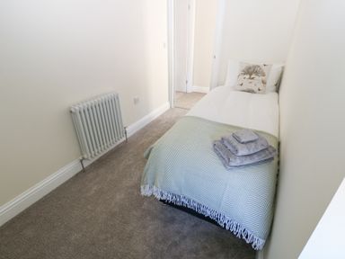 A small bedroom with a single bed a folded towel set a radiator and a doorway at Bridge End Cottage in Wark