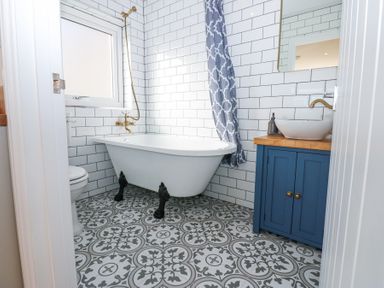 A bathroom with a clawfoot bathtub toilet and a sink with blue cabinet at Bridge End Cottage in Wark