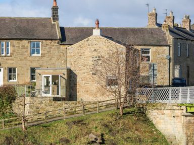 Exterior view of stone houses with chimneys a small balcony and a metal fence at Bridge End Cottage in Wark