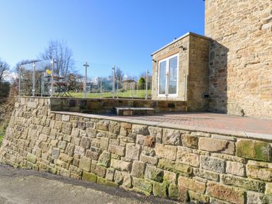 An outdoor patio area with stone walls glass railing and a small table and chairs at Bridge End Cottage in Wark