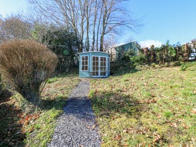 A small blue garden shed with glass doors at the end of a gravel path in a garden at Bridge End Cottage in Wark