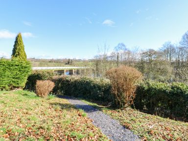 A garden path with bushes and trees near a river and bridge at Bridge End Cottage in Wark