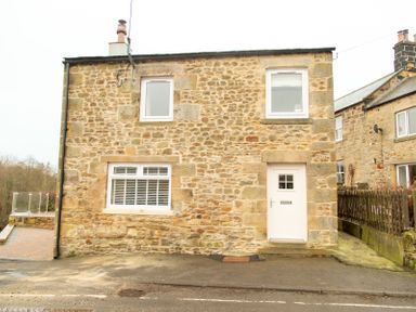 A stone house with three white framed windows and a white door at Bridge End Cottage in Wark
