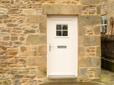 A cream colored door with a mail slot and small window set in a stone wall at Bridge End Cottage in Wark