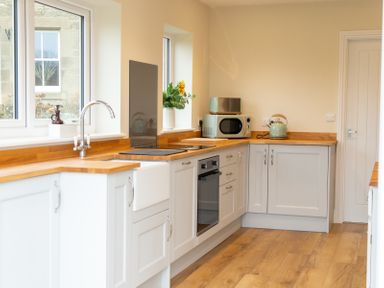 A kitchen with wooden countertops white cabinets a microwave kettle oven and sink at Bridge End Cottage in Wark