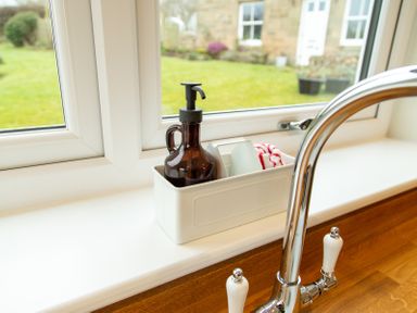 A kitchen sink faucet next to a soap dispenser and dishcloth on a windowsill overlooking a garden at Bridge End Cottage in Wark