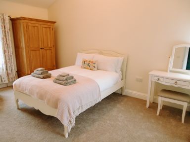 A bedroom with a bed with towels on it a wooden wardrobe and a white dressing table with a stool at Bridge End Cottage in Wark
