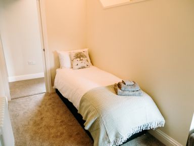 A single bed with white bedding and folded towels in a small bedroom at Bridge End Cottage in Wark