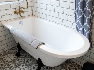 A bathroom with a white clawfoot bathtub a gray towel on the edge brass fixtures white subway tile walls and patterned floor tiles at Bridge End Cottage in Wark