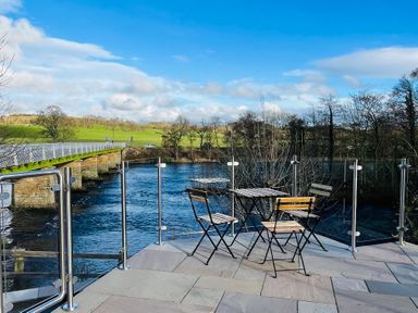 An outdoor seating area with a table and chairs near a river at Bridge End Cottage in Wark