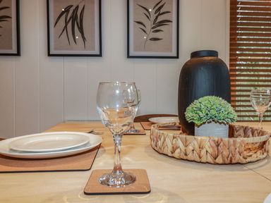 A dining table set with plates forks glasses and a woven tray with a black vase and a small green plant at 1 Streamside in Lanreath