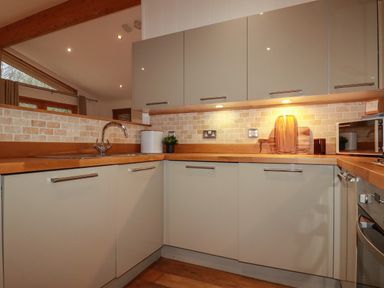 A modern kitchen with wooden countertops cabinets a sink and a microwave at 1 Streamside in Lanreath