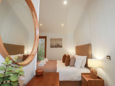 A bedroom with a bed with pillows and towels a bedside table with a lamp a round mirror and a wooden dresser at 1 Streamside Lanreath