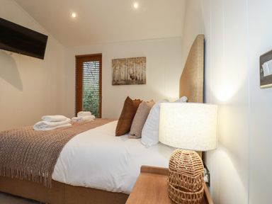 A bedroom with a bed with pillows and folded towels a lamp on a bedside table and a wall-mounted TV at 1 Streamside in Lanreath