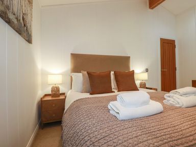 A bedroom with a bed with pillows and folded towels on a knitted blanket and bedside tables with lamps at 1 Streamside in Lanreath