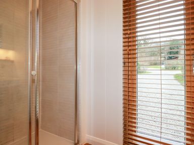 A shower enclosure with sliding glass doors next to a window with wooden blinds at 1 Streamside in Lanreath